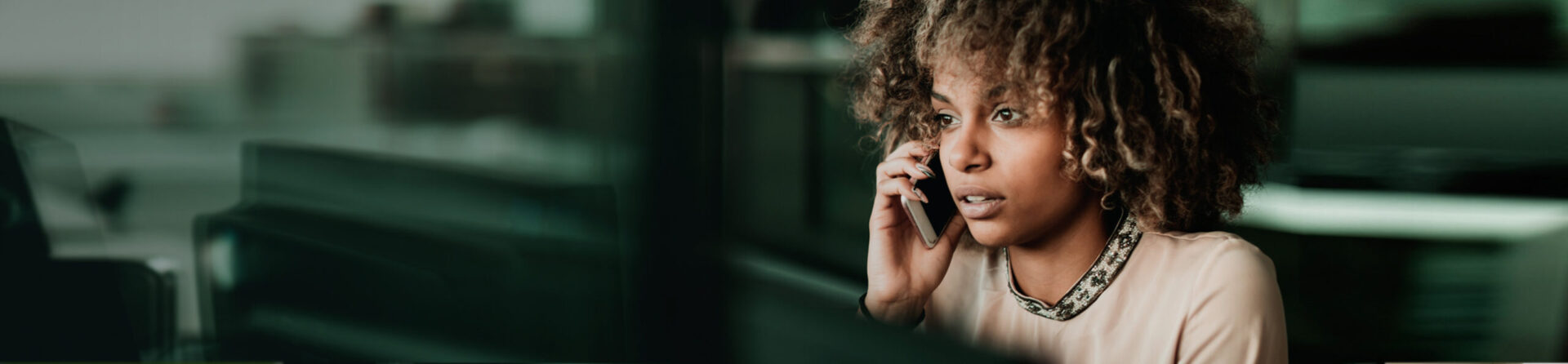 Woman on cell phone sitting at computer.