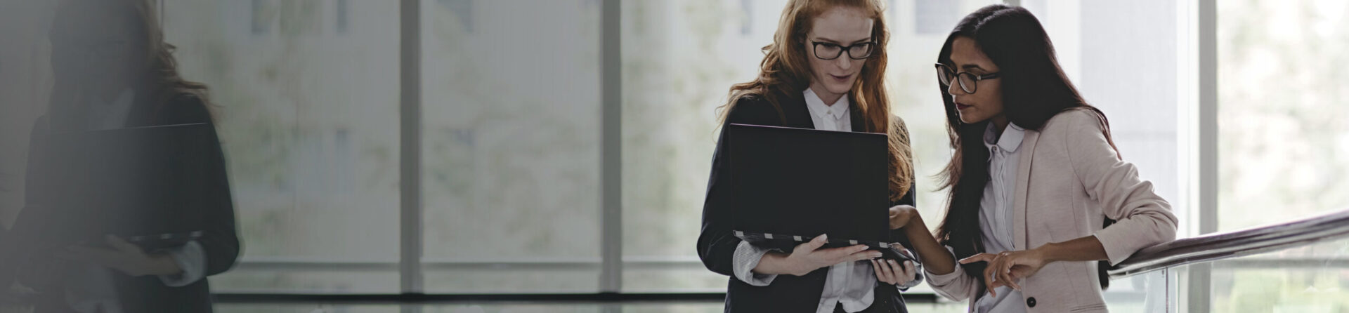 Two young professional women looking at computer by stairway.