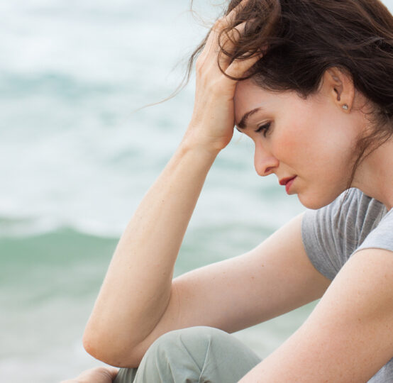 Woman sitting on beach with head in hands.